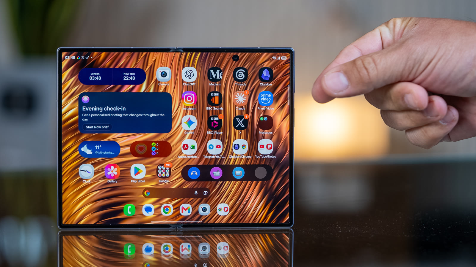 Galaxy Z Fold 8 fully open on a glass desk, inner display on, beside a stack of app-icon tiles